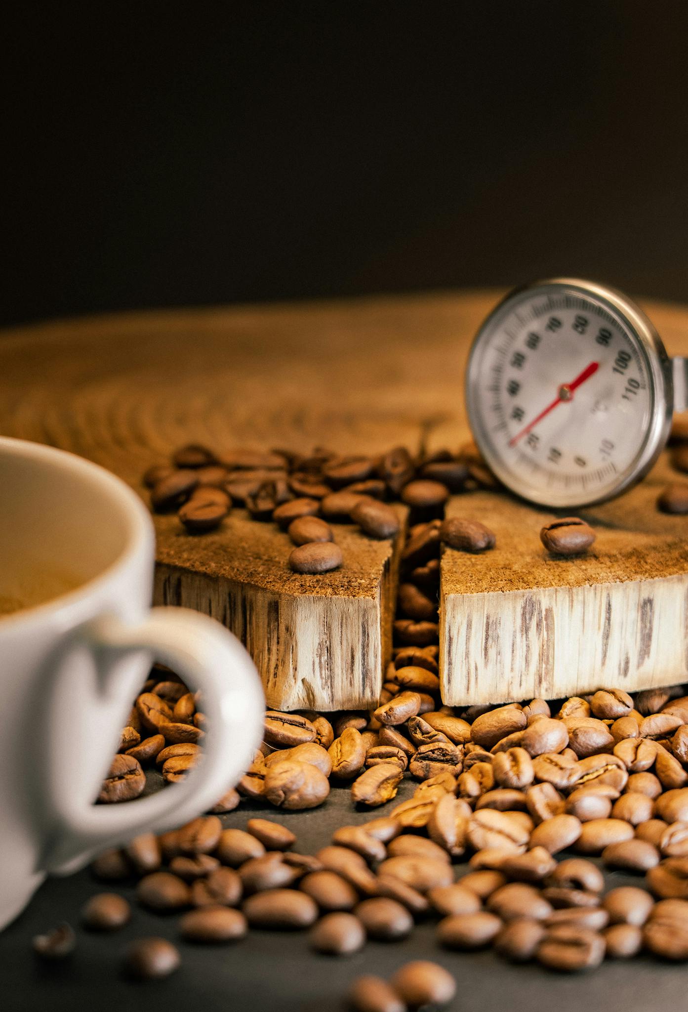 A close-up of coffee beans scattered on a wooden surface with a thermometer, evoking a rustic coffeehouse feel.