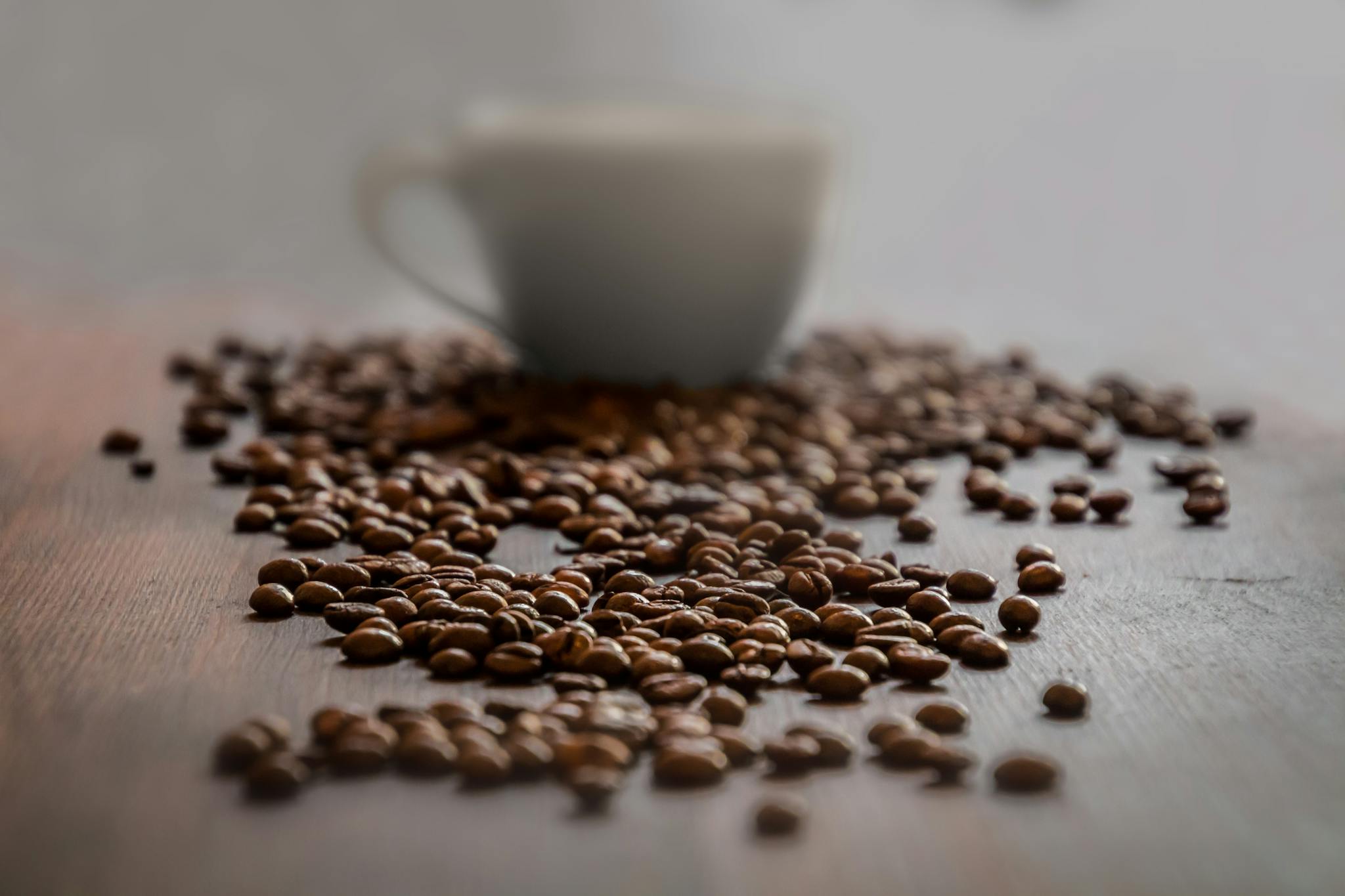 Close-up of coffee beans scattered around a cup on a wooden table.